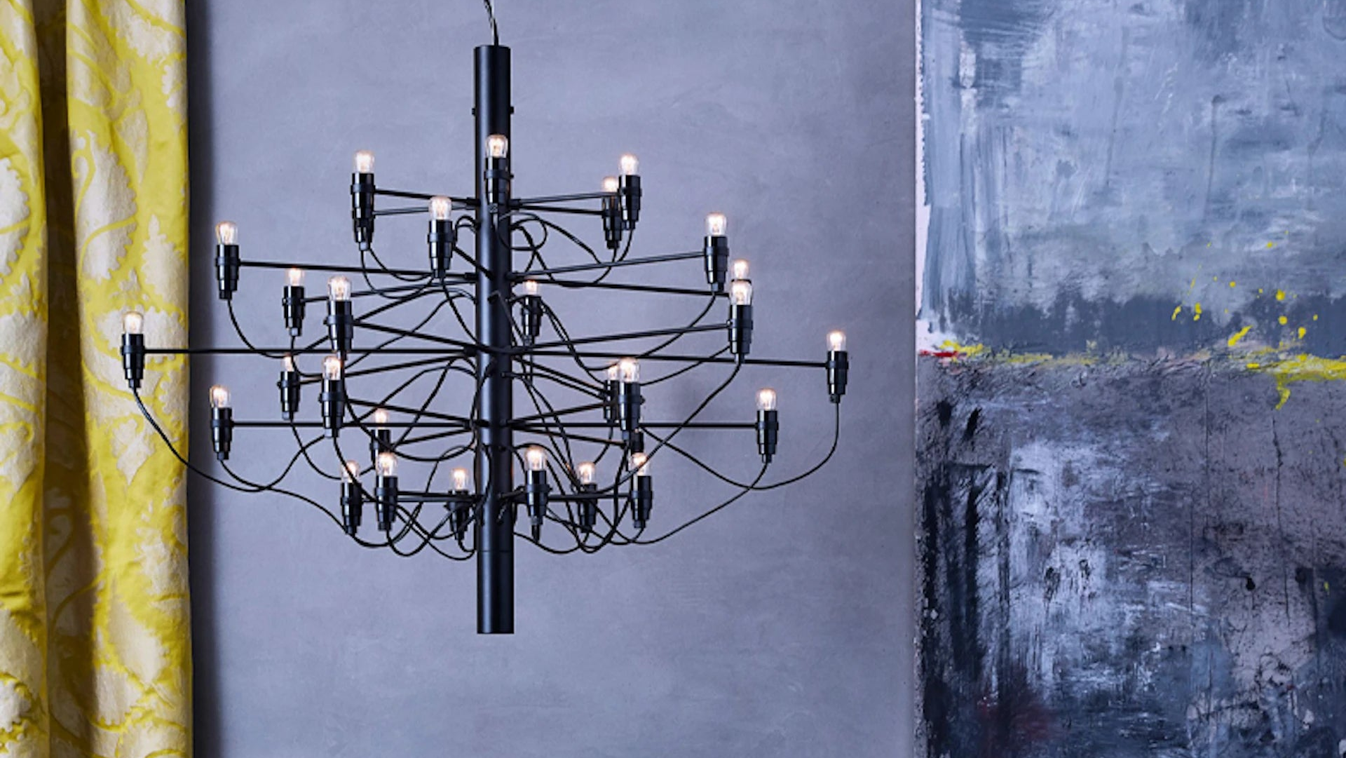 Black chandelier hanging against a textured wall with abstract art.