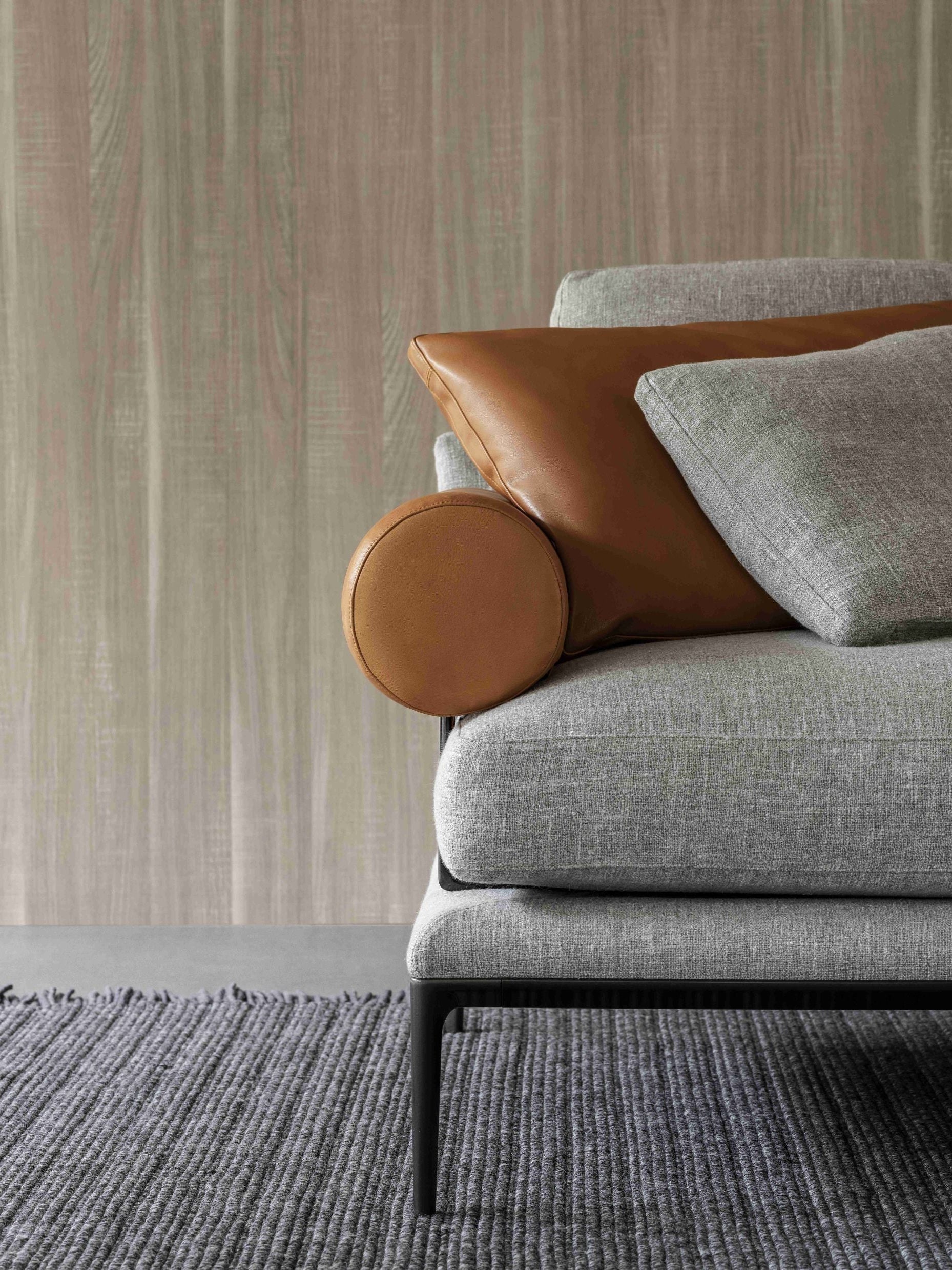 Gray sofa with brown and gray cushions against a textured wall.