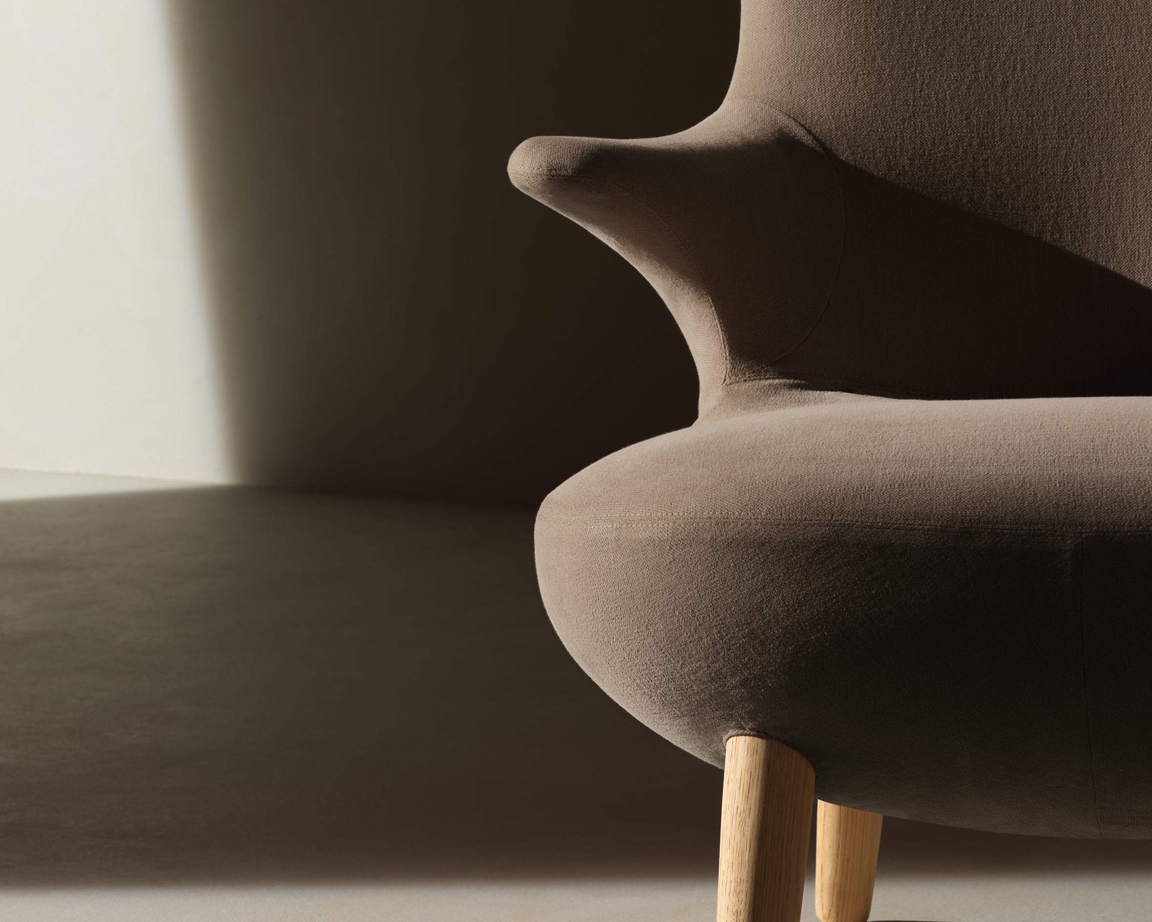 Brown upholstered chair with wooden legs against a dark background