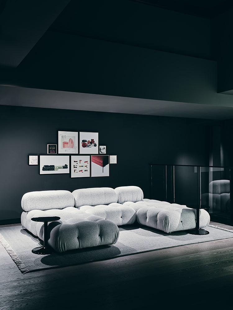 Modern white sofa in a dark room with framed pictures on the wall.