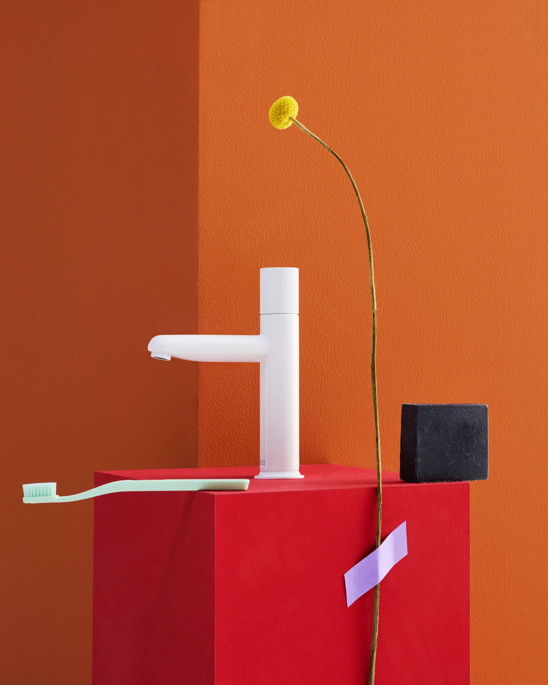 White faucet on a red stand with a yellow flower against an orange background